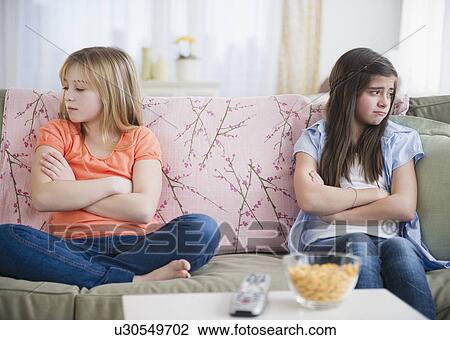 Stock Image - Two girls sitting on sofa and showing disgust. Fotosearch