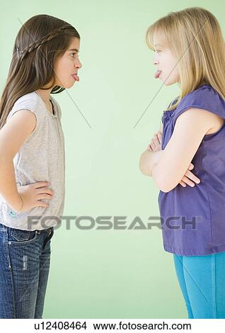 Picture -  Two girls standing face to face and sticking out tongues. Fotosearch