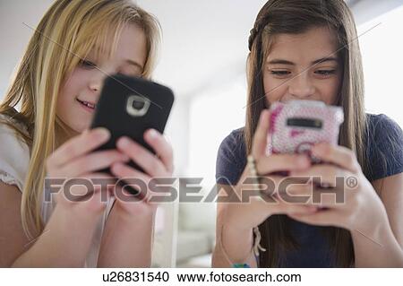 Two girls texting on smart phones View Large Photo Image Stock Image - Two girls texting on smart phones. Fotosearch