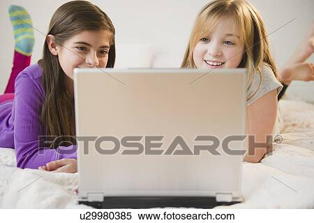 Two girls using laptop on bed View Large Photo Image Stock Photography - Two girls using laptop on bed. Fotosearch