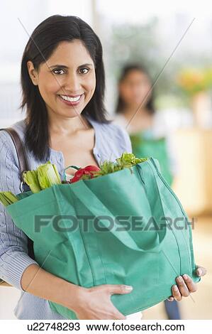 Stock Image - Woman holding bag of fresh vegetables. Fotosearch