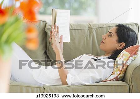Stock Image - Woman reading book on sofa. Fotosearch