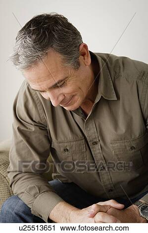 Stock Image - Worried mature man sitting on sofa. Fotosearch
