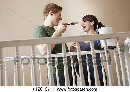 Stock Photo - Young couple standing face to face holding paint brush. Fotosearch