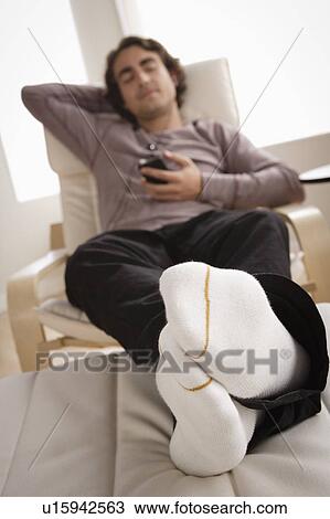 Stock Image - Young man listening music on armchair. Fotosearch