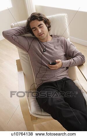 Stock Photo - Young man listening music on armchair. Fotosearch