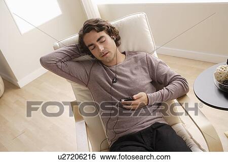 Young man listening music on armchair View Large Photo Image Stock Photograph - Young man listening music on armchair. Fotosearch
