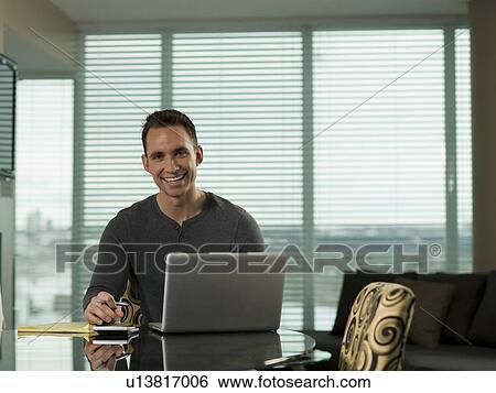 Young man paying bills at kitchen table View Large Photo Image Stock Photograph - Young man paying bills at kitchen table. Fotosearch
