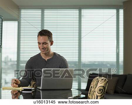 Stock Photography - Young man paying bills at kitchen table. Fotosearch