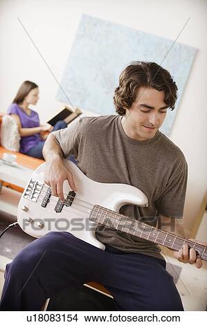Young man playing electric guitar, young woman in background View Large Photo Image Picture - Young man playing electric guitar, young woman in background. Fotosearch