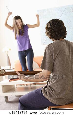 Stock Image - Young man playing electric guitar, young woman dancing in background. Fotosearch