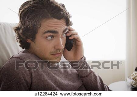 Young man sitting on armchair and talking via mobile View Large Photo Image Picture - Young man sitting on armchair and talking via mobile. Fotosearch