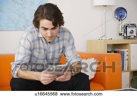 Young man sitting on sofa and using digital tablet View Large Photo Image Stock Photo - Young man sitting on sofa and using digital tablet. Fotosearch