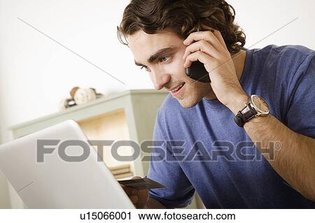 Stock Image - Young man talking via mobile at home. Fotosearch