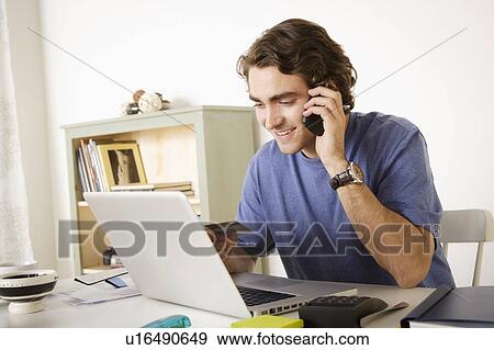 Stock Photo - Young man talking via mobile at home. Fotosearch