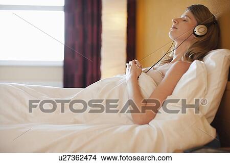 Picture - Young pregnant woman listening to music in bed. Fotosearch