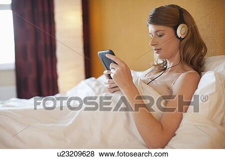 Stock Photo - Young pregnant woman listening to music in bed. Fotosearch