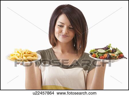 Picture - Young woman choosing between healthy and unhealthy food. Fotosearch