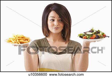 Stock Image - Young woman choosing between healthy and unhealthy food. Fotosearch