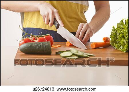 Stock Image - Young woman cutting vegetables. Fotosearch