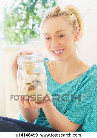 Stock Photo - Young woman holding shells in jar. Fotosearch