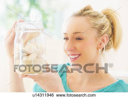 Stock Photograph - Young woman holding shells in jar. Fotosearch