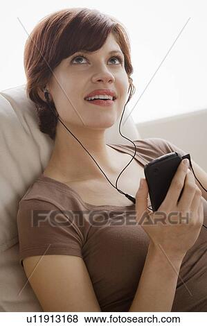 Stock Photo - Young woman listening music on armchair. Fotosearch