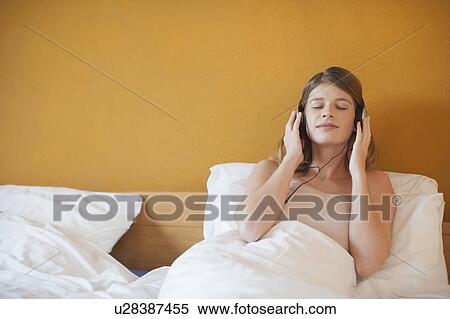 Stock Photography - Young woman listening to music in bed. Fotosearch