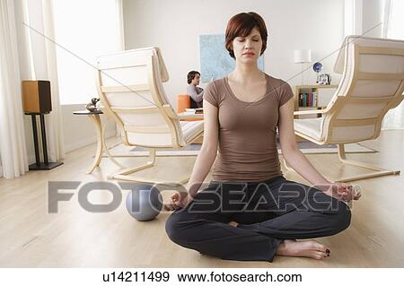 Stock Photo - Young woman meditating, man relaxing in background. Fotosearch