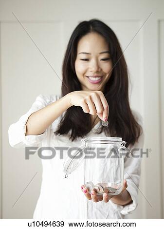 Young woman putting coin into jar View Large Photo Image Stock Photo - Young woman putting coin into jar. Fotosearch