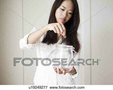 Young woman putting coin into jar View Large Photo Image Stock Photo - Young woman putting coin into jar. Fotosearch