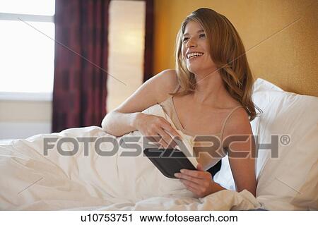 Young woman reading on an e-reader in bed View Large Photo Image Stock Image - Young woman reading on an e-reader in bed. Fotosearch