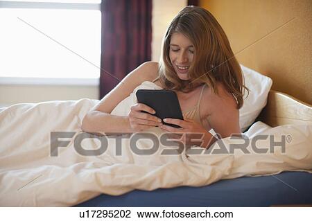 Stock Image - Young woman reading on an e-reader in bed. Fotosearch