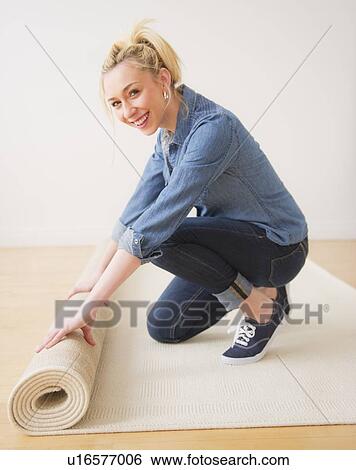 Stock Photograph - Young woman rolling up carpet, studio shot. Fotosearch