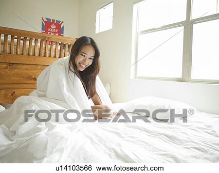 Stock Photograph - Young woman sitting on bed. Fotosearch