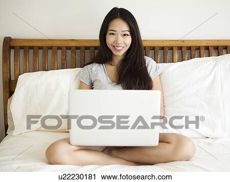 Young woman sitting on bed, using laptop View Large Photo Image Stock Image - Young woman sitting on bed, using laptop. Fotosearch