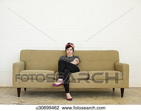 Stock Image - Young woman sitting on sofa. Fotosearch