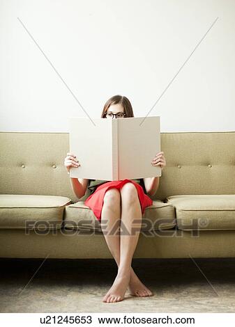 Young woman sitting on sofa with book View Large Photo Image Stock Image - Young woman sitting on sofa with book. Fotosearch