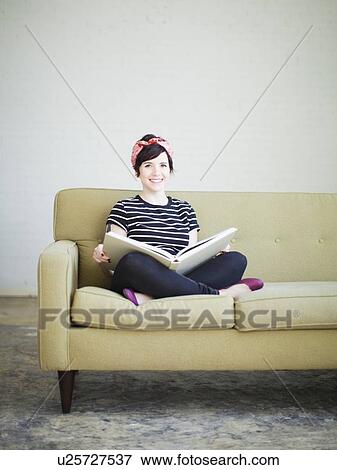 Stock Photo - Young woman sitting on sofa with book. Fotosearch