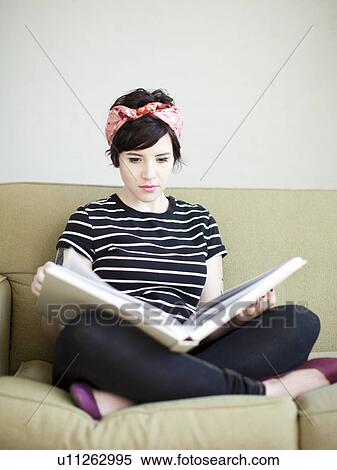 Stock Photography - Young woman sitting on sofa with book. Fotosearch