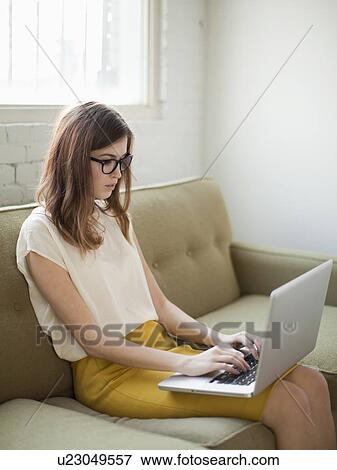 Young woman sitting on sofa with laptop View Large Photo Image Stock Photo - Young woman sitting on sofa with laptop. Fotosearch