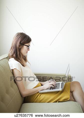 Stock Photograph - Young woman sitting on sofa with laptop. Fotosearch