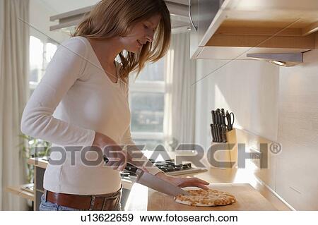 Stock Photo - Young woman slicing pizza. Fotosearch