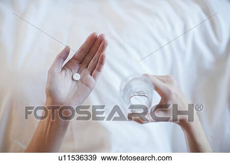 Stock Photo - Young woman taking medicine while lying in bed . Fotosearch