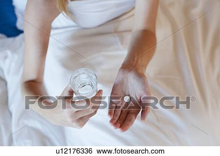 Stock Photograph - Young woman taking medicine while lying in bed . Fotosearch
