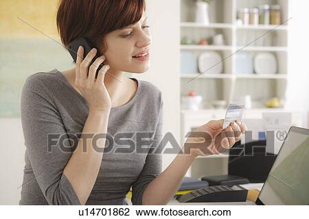 Stock Image - Young woman talking via mobile at home. Fotosearch