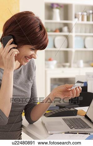 Stock Image - Young woman talking via mobile at home. Fotosearch