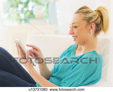 Stock Image - Young woman using digital tablet on sofa. Fotosearch