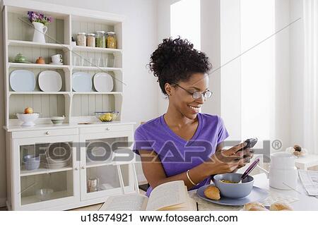 Stock Image - Young woman using mobile at breakfast. Fotosearch