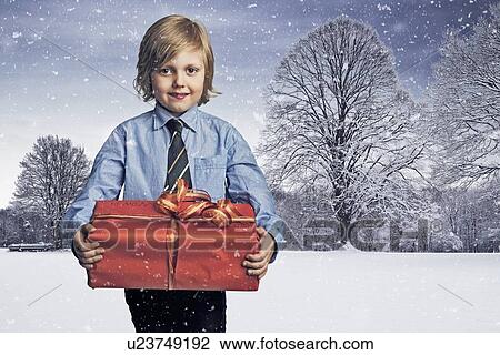 Stock Image - Boy carrying Christmas gift in snow. Fotosearch